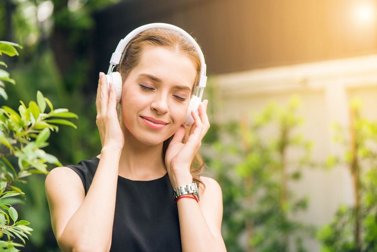 Mujer sonriente con los ojos cerrados disfrutando de la música en un jardín soleado