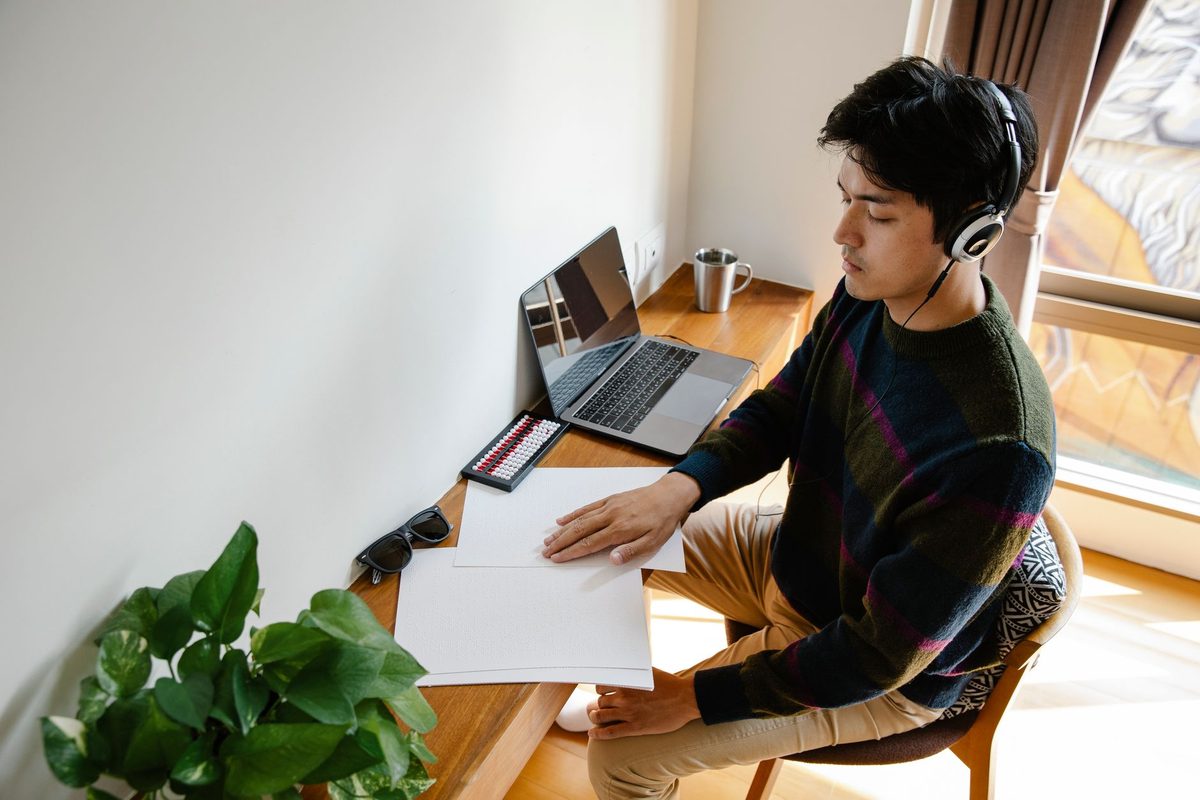 Joven con auriculares estudiando en su mesa junto a la ventana