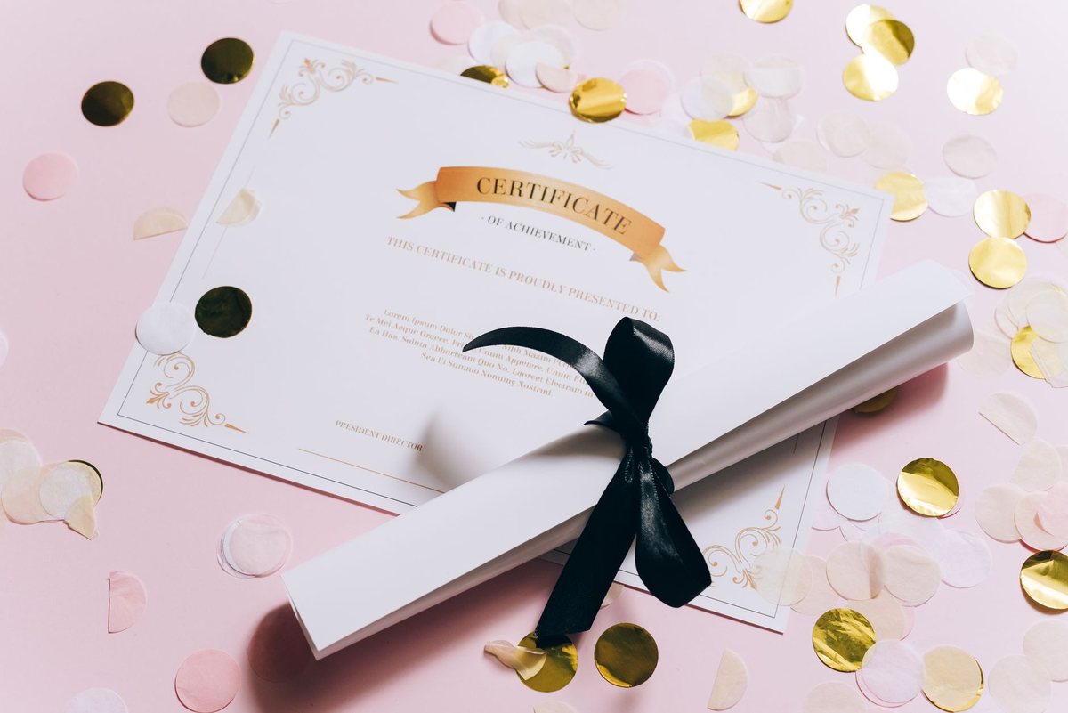 Un diploma enrollado con una cinta negra, sobre confeti dorado y rosa