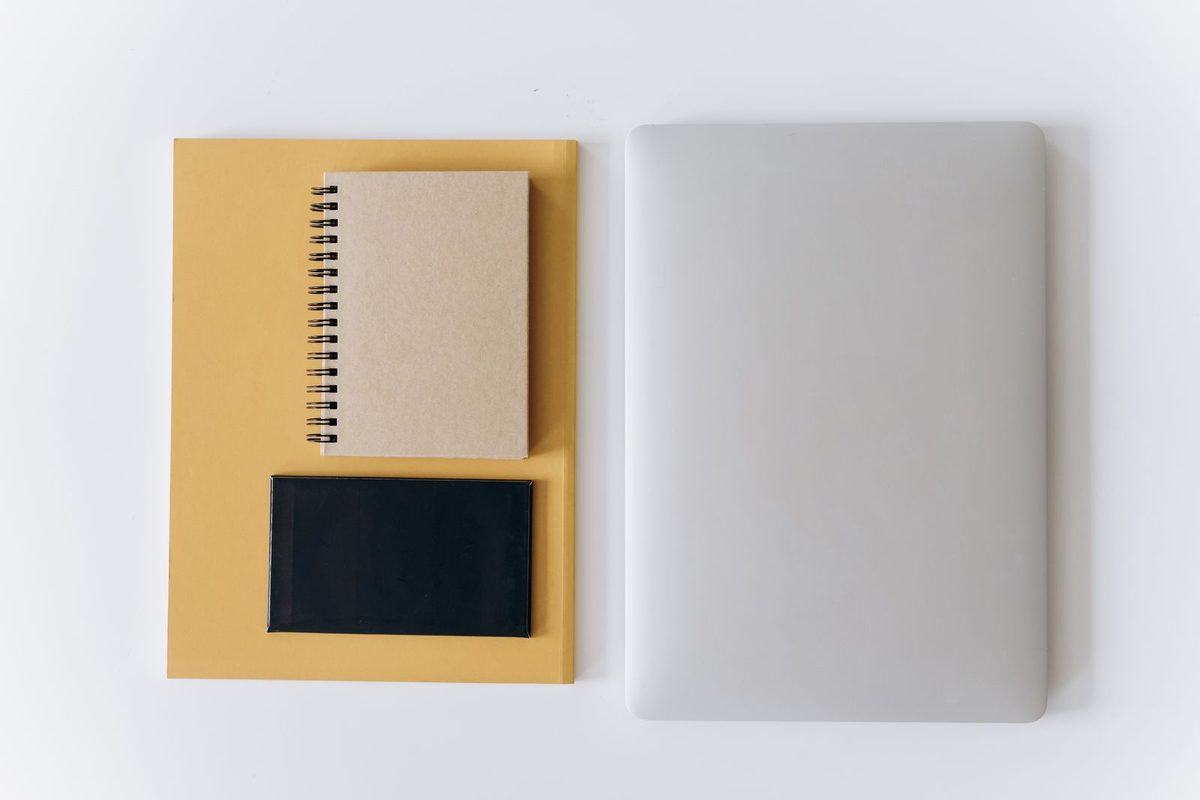 Portátil cerrado junto a una carpeta y dos cuadernos sobre una mesa blanca