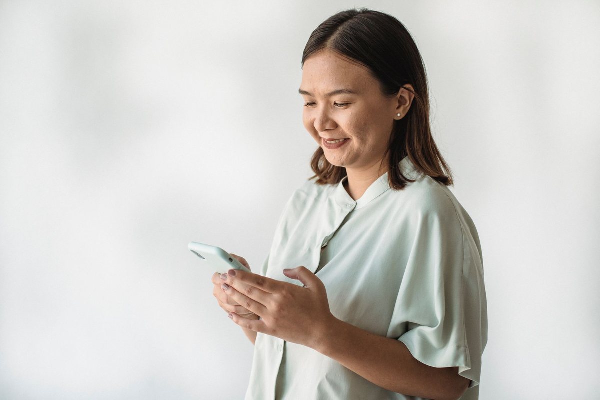 Una mujer sonriente mirando la pantalla de su teléfono móvil, sobre fondo claro