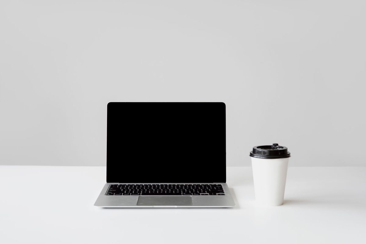 Portátil abierto y vaso de café sobre un escritorio blanco