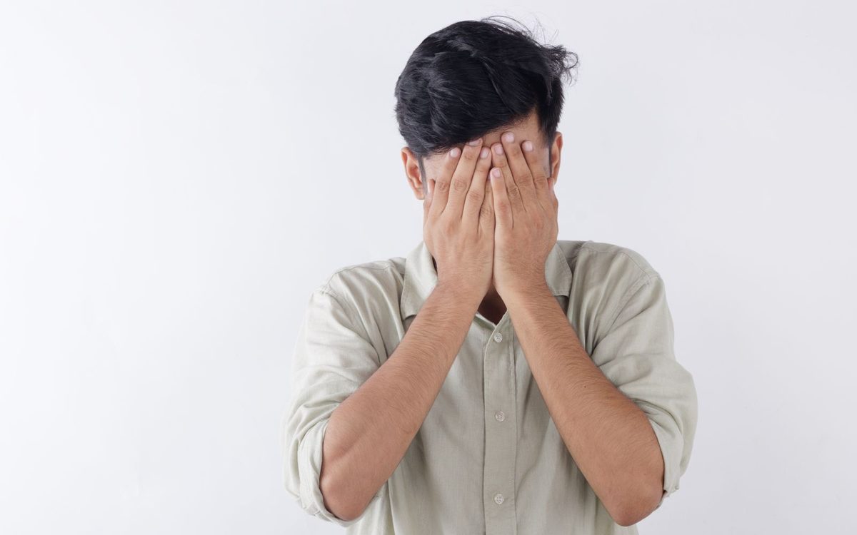 Hombre tapándose la cara con las manos por vergüenza sobre fondo blanco