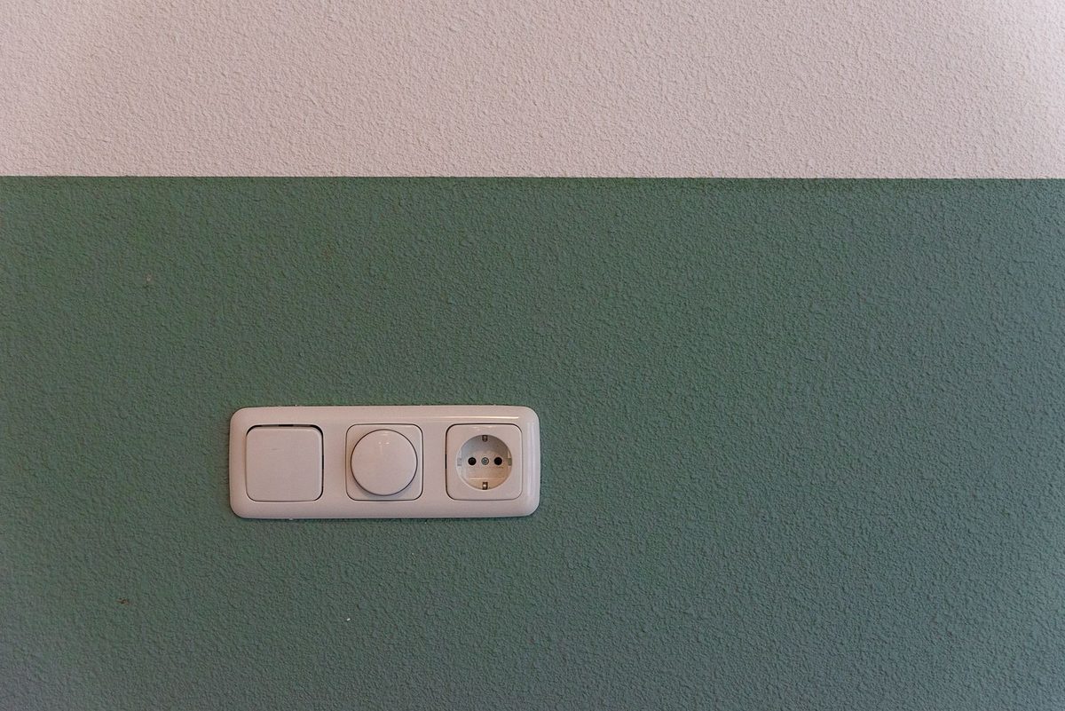 Enchufe y dos interruptores blancos en una pared verde y blanca