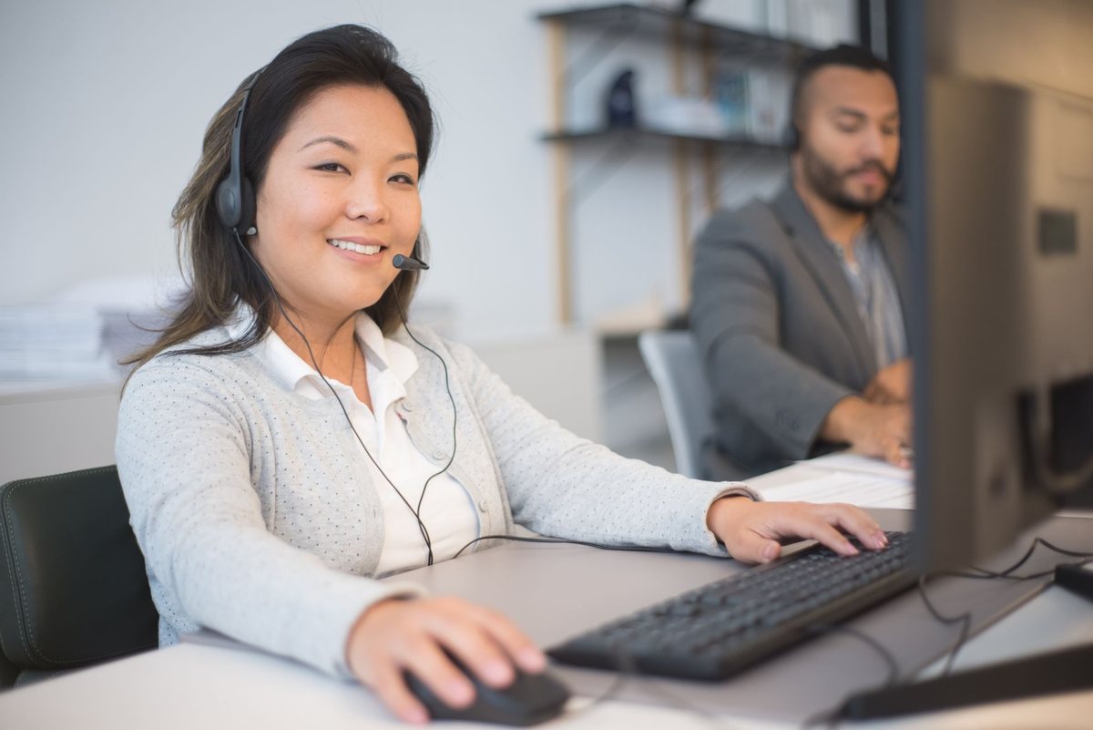 Una mujer con auriculares de atención telefónica sonriendo frente al ordenador