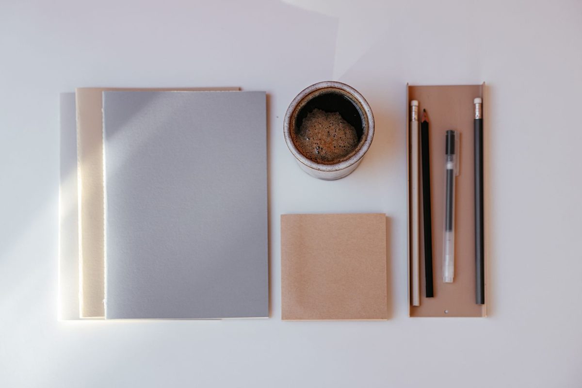 Cuadernos, taco de notas, lápices y una taza de café ordenados sobre una mesa blanca