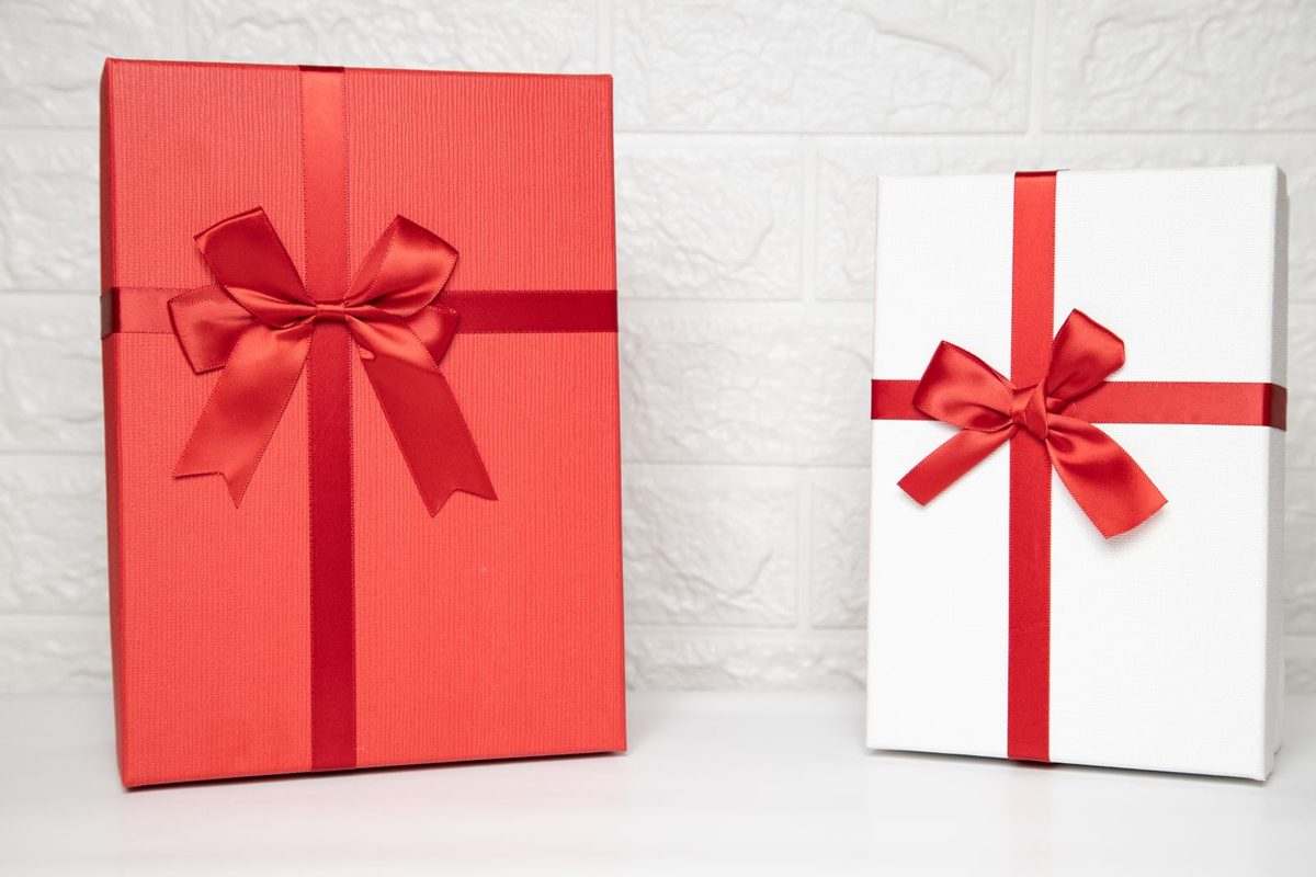 Dos cajas de regalo, una roja y otra blanca, con lazos rojos sobre fondo blanco
