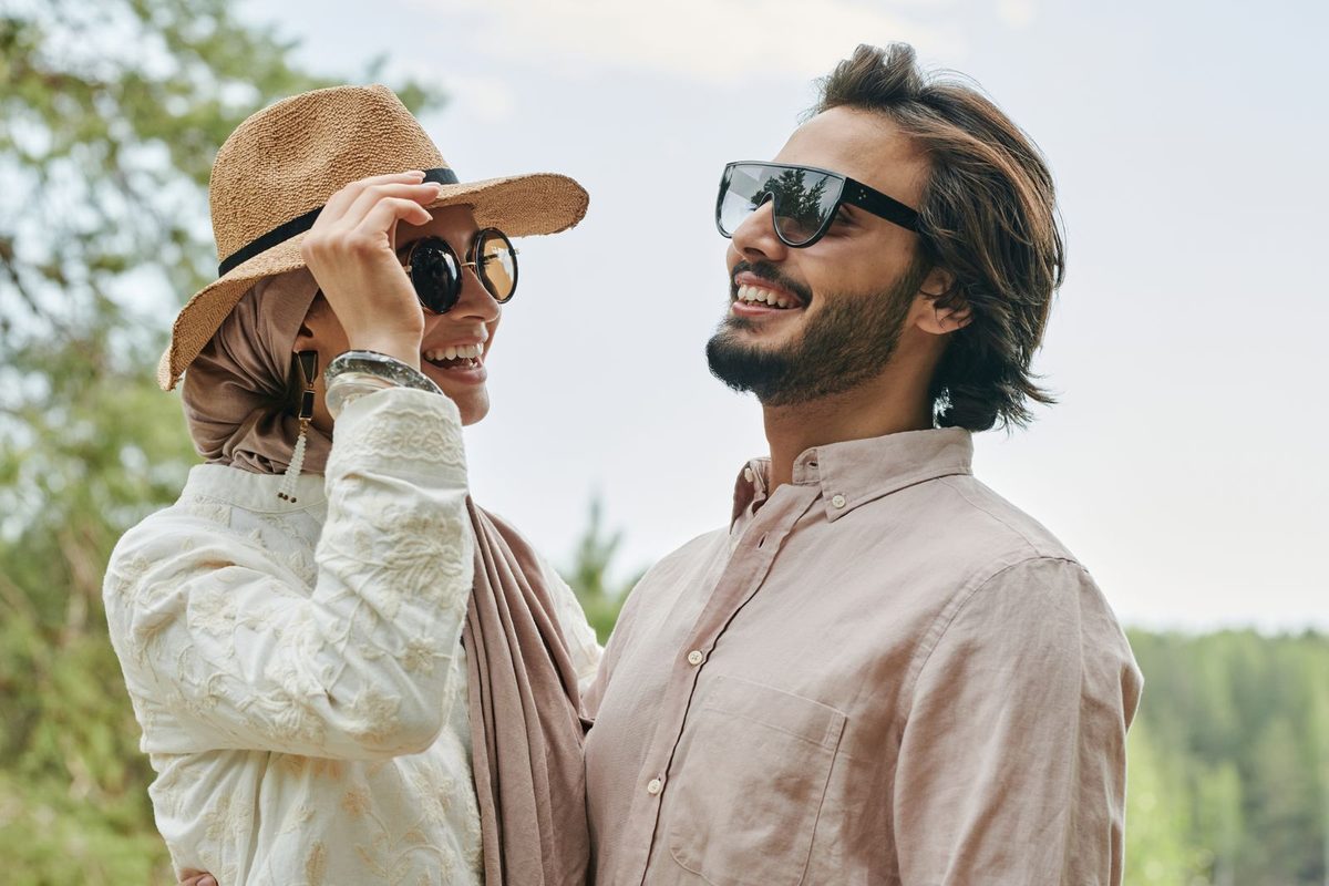 Pareja riéndose al aire libre con sombrero y gafas de sol