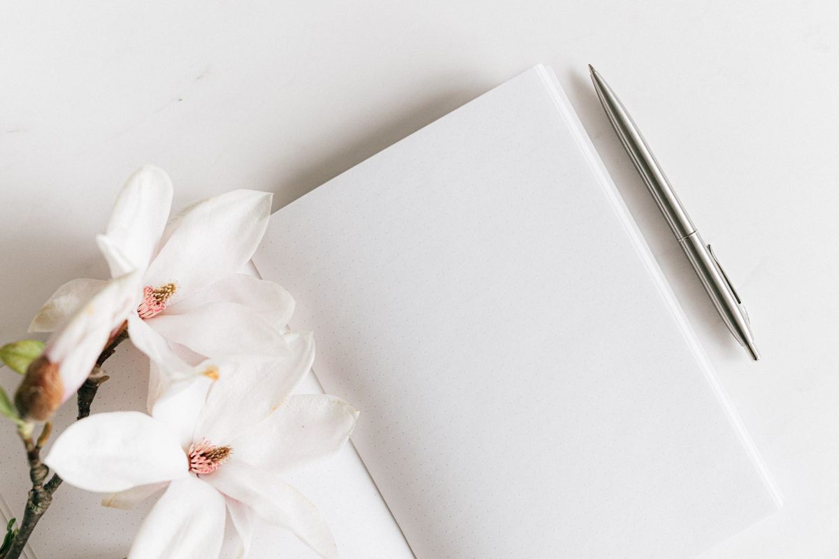 Cuaderno en blanco con un bolígrafo plateado y flores de magnolia