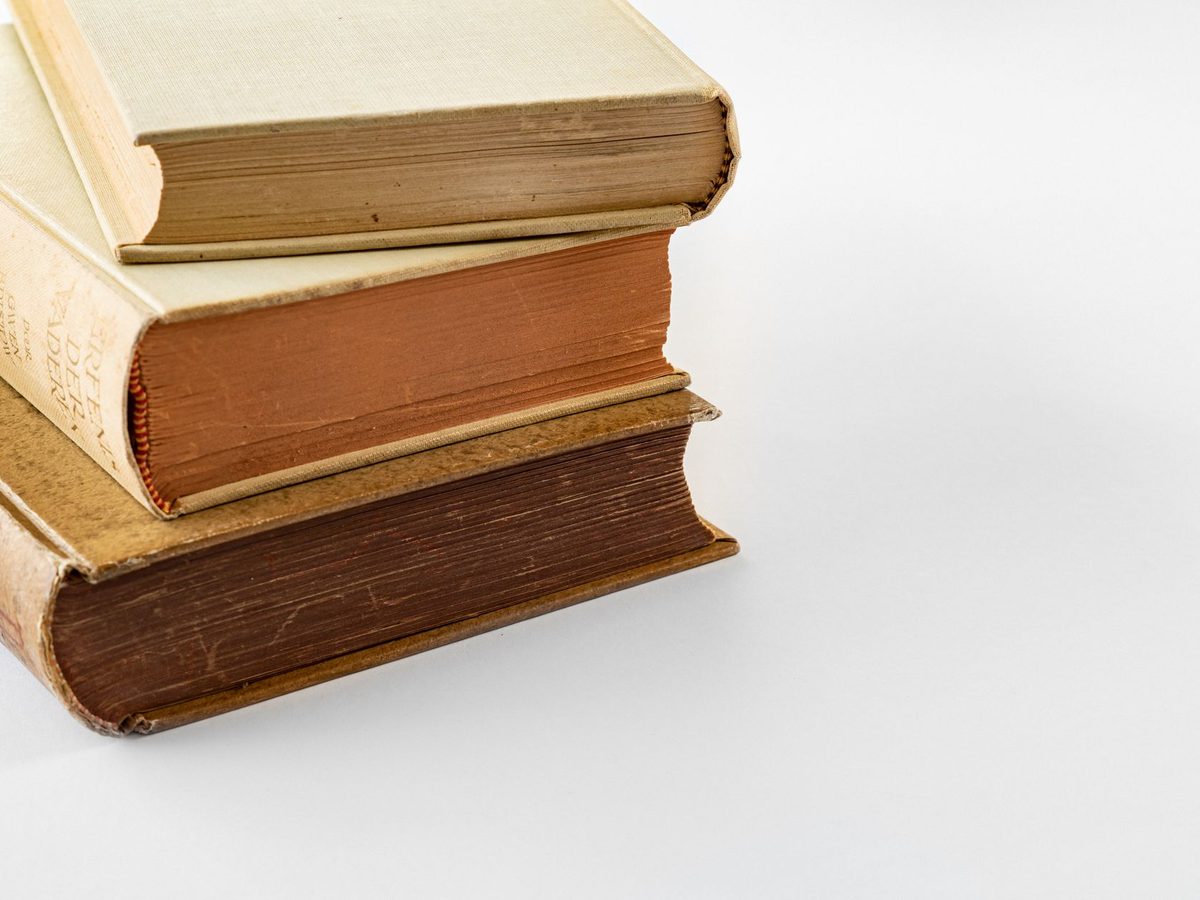 Tres libros antiguos apilados sobre fondo blanco