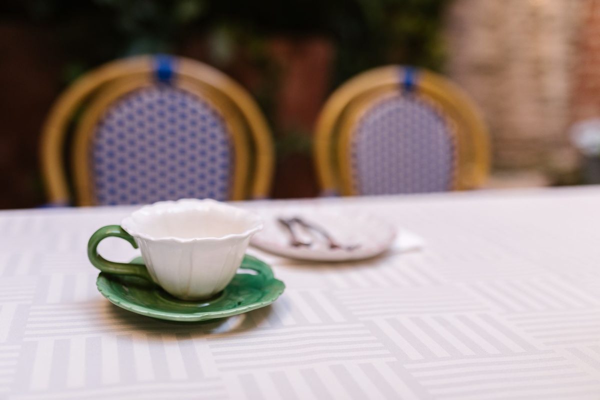 Taza de café vacía y plato de postre con cubiertos sobre un mantel claro a la luz del día