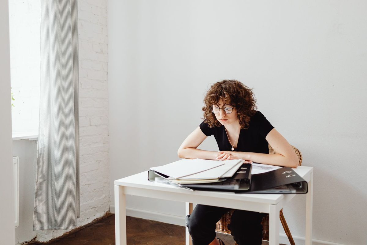 Mujer revisando carpetas con gesto reflexivo en una mesa blanca