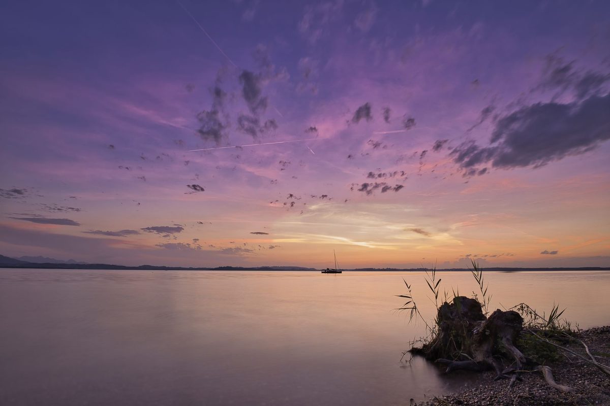 Cielo malva al atardecer sobre un lago en calma con un velero a lo lejos